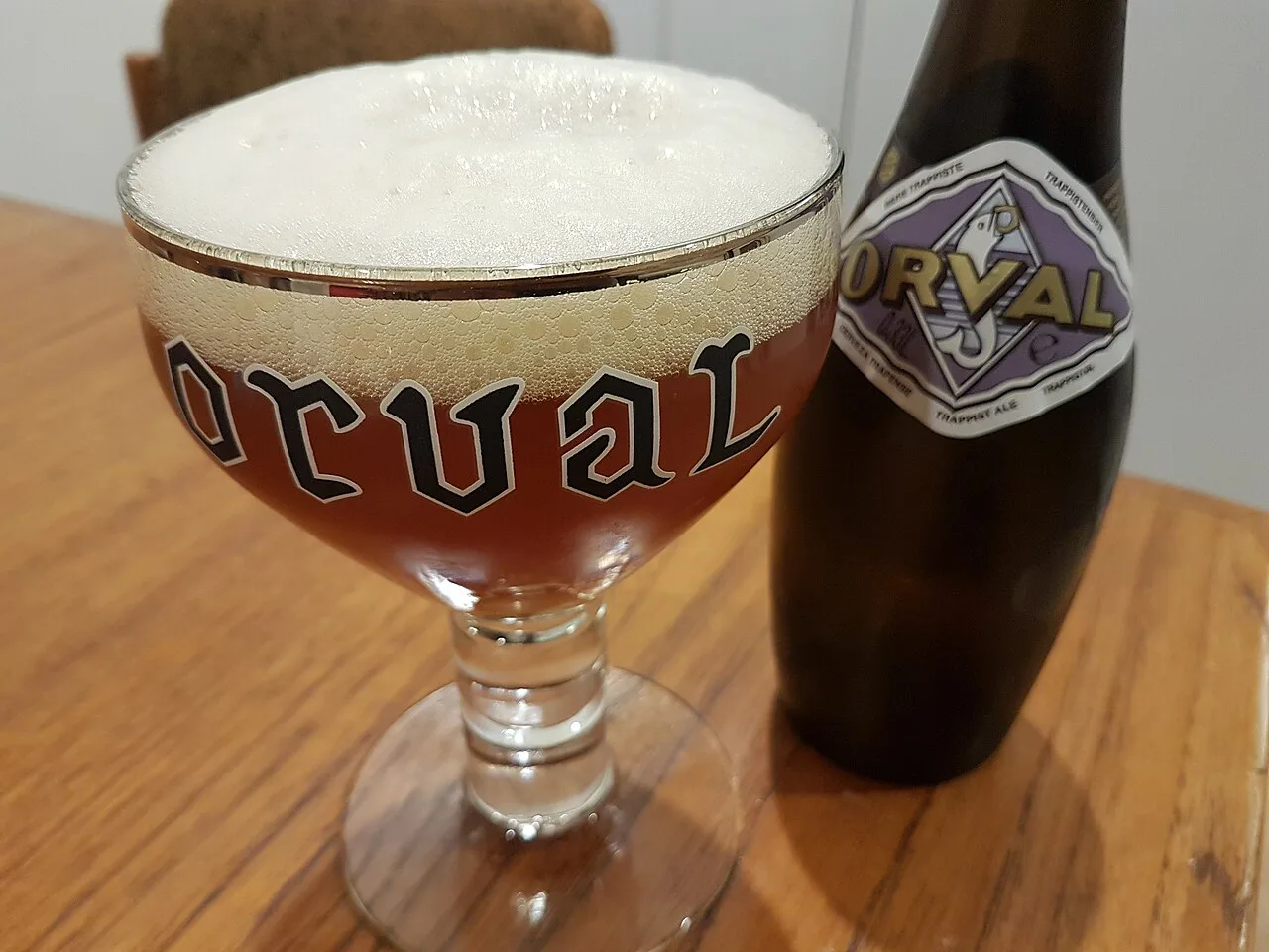 A bottle of Orval Trappist ale beside its traditional chalice glass.