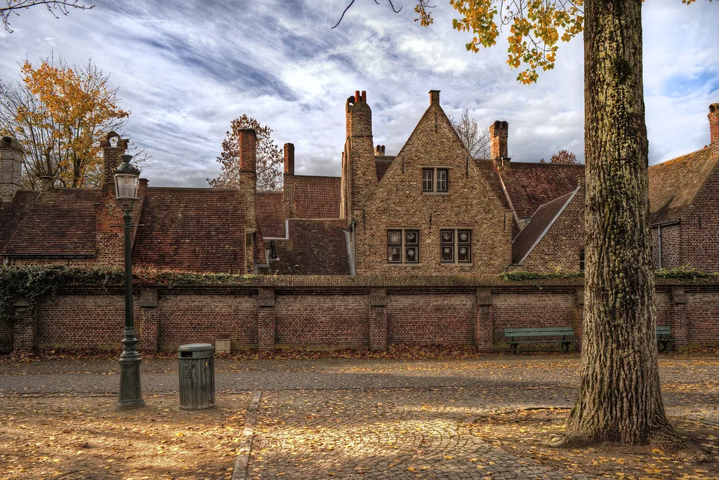 Old brick buildings behind a wall under autumn trees in Bruges.