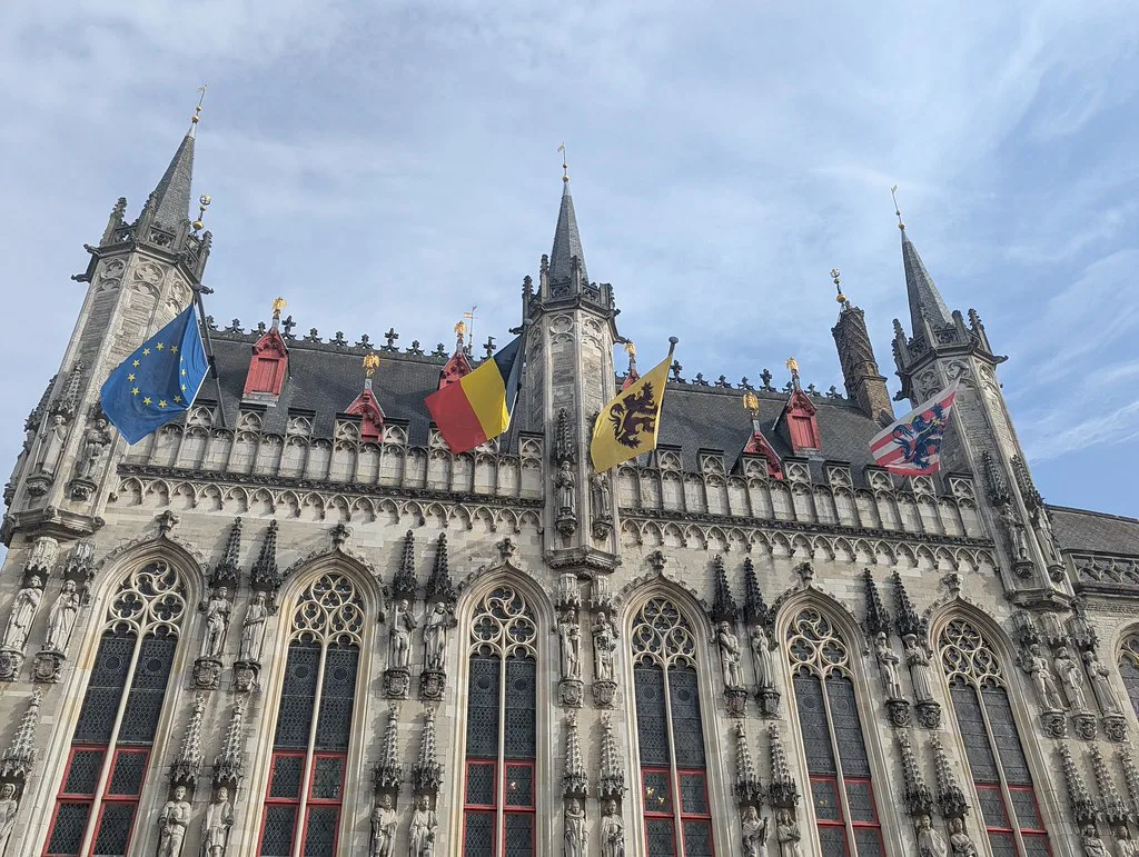 The Gothic facade of Bruges City Hall on the Burg under a blue sky.