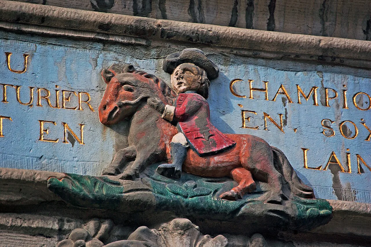 A painted shop-sign relief of a rider, Au Champion, on a façade in Rue Hors-Château, Liège.