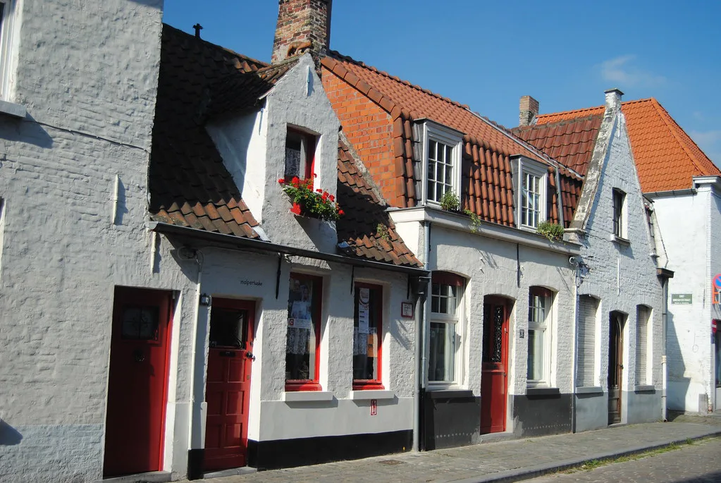 A row of low whitewashed houses with red doors on a quiet street in Bruges.