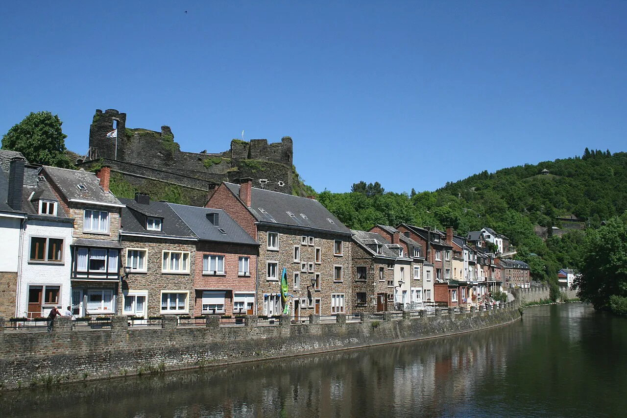Houses lining the River Ourthe in La Roche-en-Ardenne, with the castle ruins on the wooded hill above.